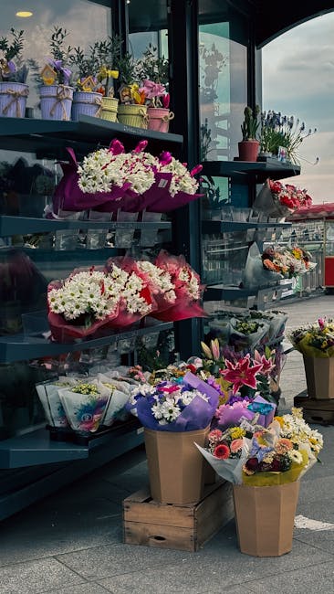 A display of various floral arrangements at Malden Rushett Florist, showcasing vibrant bouquets wrapped in colorful paper and cellophane. The flowers include white chrysanthemums, pink lilies, purple