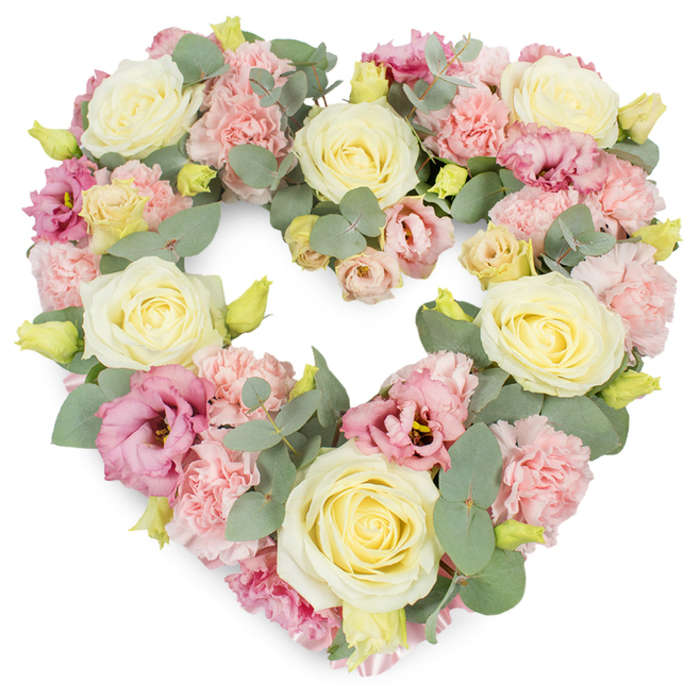 A detailed image shows a heart-shaped floral tribute resting against a pure white background, its entire surface richly covered with pastel blooms and cool foliage. The heart is symmetrical and clearly defined, with an unbroken edge made up of petals and leaves that flow smoothly from one to the next. At intervals around the heart, large cream and pale lemon roses act as graceful focal points, their velvety petals tightly layered at the centre before relaxing into broader outer petals that create soft highlights and shadows. Between and around these roses, clusters of light pink carnations fill the design, their ruffled, almost lace-like texture giving the wreath a plush, cushioned appearance that feels tender and welcoming. Deeper tones appear in the form of pink and mauve lisianthus, whose slightly more open, cup-shaped blooms introduce gentle depth and hints of shadow, drawing the eye inward. Threaded delicately through the flowers, silvery eucalyptus leaves with their rounded, blue-green discs provide contrast and structure, their cool tones balancing the warmth of the creams and pinks. Little yellow-green buds punctuate the design, suggesting freshness and the continuation of life, even as the piece speaks of farewell. The arrangement is densely packed, with no visible gaps, reflecting experienced craftsmanship and a sense of loving attention, as if arranged by a florist who often serves families in Malden Rushett and along the nearby country lanes. This heart-shaped wreath feels particularly suited to funeral services, cremations, or memorial gatherings, a calm and beautiful way to honour a special person with a symbol of love, remembrance, and enduring connection.